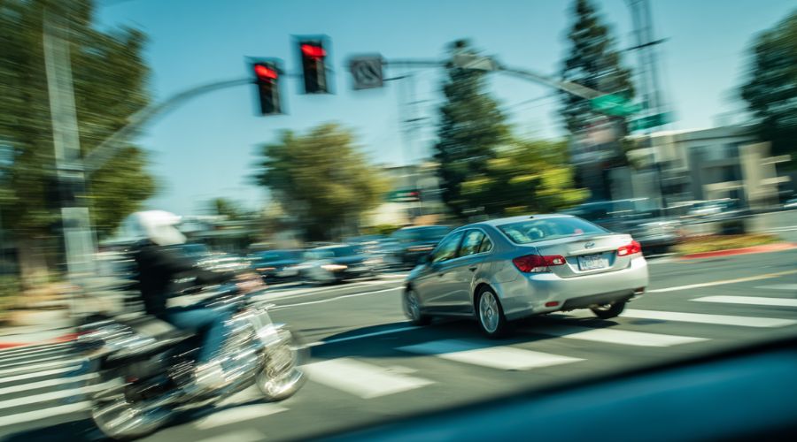 Motorcycle Accidents in Southern California: Legal Rights Explained 1 A car making a left turn at a busy California intersection as an approaching motorcyclist brakes to avoid impact, urban street with traffic lights and crosswalk, motion blur conveying sudden danger, daylight