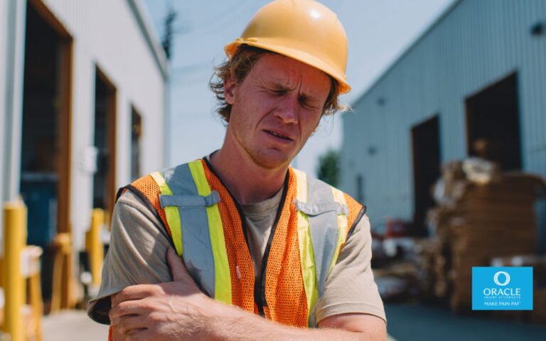 Injured worker wearing a hard hat and safety vest standing outside a warehouse in Orange County, holding arm in mild pain, worksite visible in background, daylight