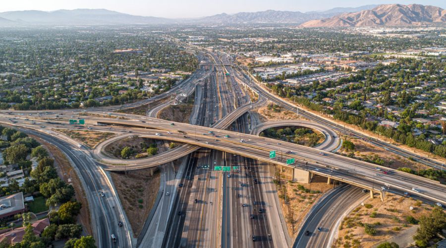 elevated view of a complex Inland Empire highway interchange with multiple merging lanes, heavy traffic flow, cars entering and exiting ramps, clear signage, bright daylight