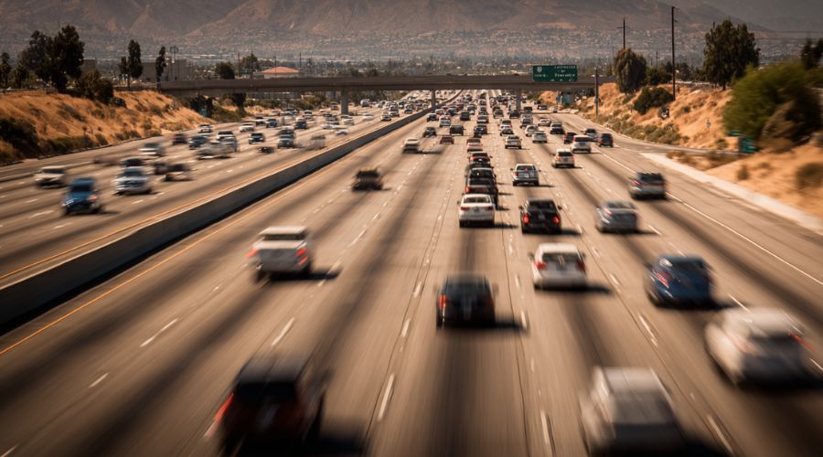 Photo of heavy traffic on an Inland Empire freeway such as I-10 or I-15, cars traveling at high speeds, long straight roadway, clear sky, commuters driving, subtle motion blur, Southern California desert surroundings