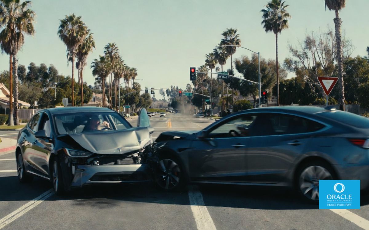 7,1 s Escena realista de un accidente de tráfico en una intersección suburbana de Yorba Linda, California, a plena luz del día. Dos vehículos modernos se ven involucrados en una colisión leve: uno intenta girar a la izquierda y el otro sigue recto. El entorno incluye palmeras, casas, semáforos y señalización vial clara. Un ligero efecto de movimiento borroso sugiere un impacto repentino, mientras que dentro de uno de los vehículos se ve a un conductor distraído usando el teléfono móvil.