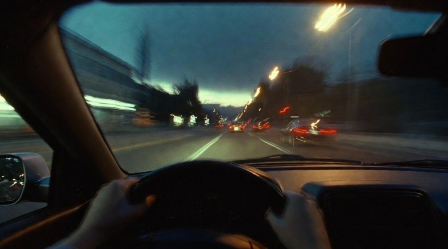 What Are the Most Common Causes of Car Accidents in Irvine? 2 Point-of-view shot from inside a car showing blurred and distorted vision of a city street at night, traffic lights and headlights appearing hazy, steering wheel in foreground, illustrating impaired driving perception, realistic cinematic style