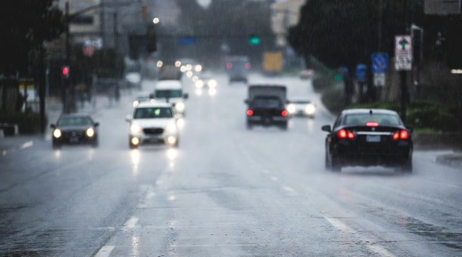 Cars driving on a wet road during light rain in Southern California, reflections on pavement, reduced visibility, vehicles moving cautiously, realistic weather conditions, cinematic realism