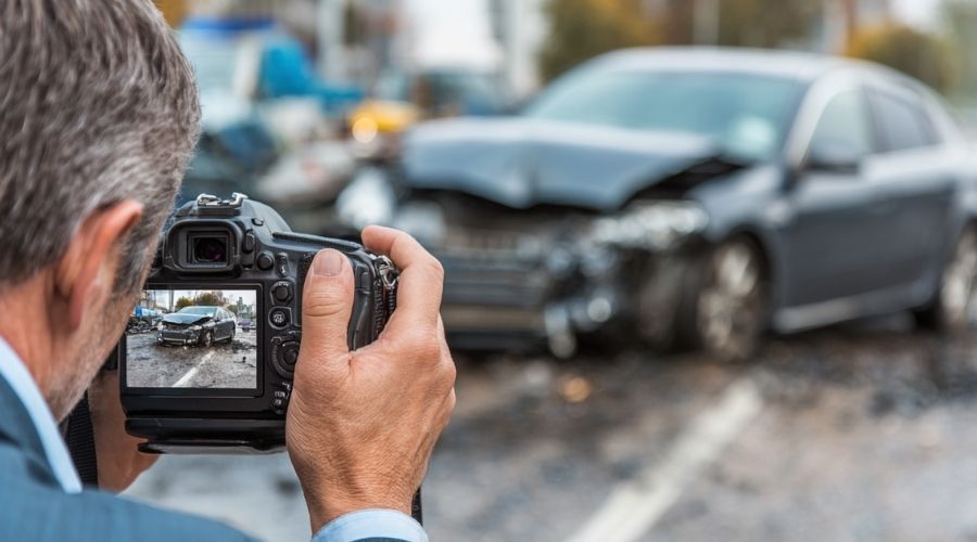 Abogado de lesiones personales que fotografía la escena de un accidente con una cámara y documenta las marcas de derrape y los daños del vehículo, en un ambiente de investigación legal profesional.