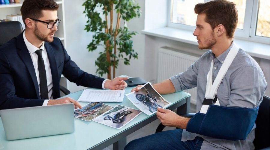 What to Do After a Motorcycle Accident in Orange County 3 Professional personal injury lawyer meeting with an injured motorcyclist in a modern office, client wearing an arm sling reviewing accident photos and documents with attorney, supportive and professional consultation, natural lighting, realistic legal setting