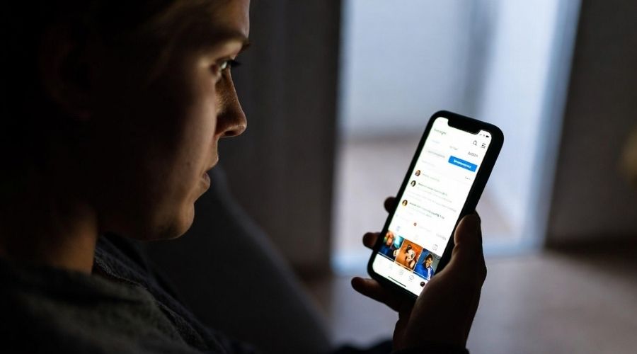 What to Do After a Car Accident in Lake Forest, California 3 A person looking at their phone with a worried expression, social media app visible on screen, dim indoor lighting, symbolic of hesitation and decision-making.