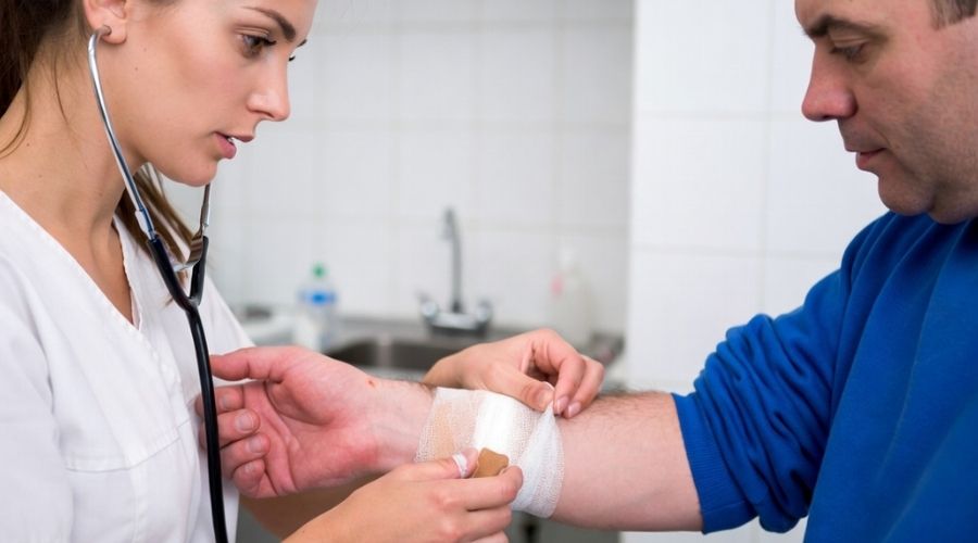 Una enfermera venda la muñeca lesionada de un trabajador en una clínica, un entorno médico luminoso y limpio, una atmósfera tranquilizadora, un estilo realista.