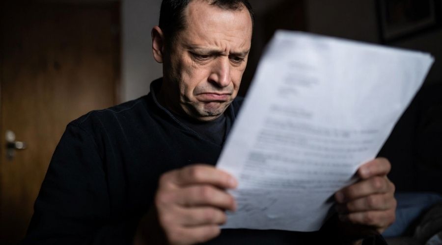 Un trabajador frustrado leyendo una carta con expresión seria, iluminación tenue con sombras para enfatizar el estrés, ambiente doméstico, realismo cinematográfico, gran nivel de detalle.,
