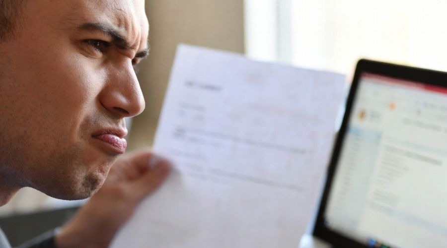 Cuándo contratar a un abogado de lesiones personales después de un accidente automovilístico en Murrieta 2 Primer plano de una persona con expresión escéptica mientras revisa un documento de oferta de acuerdo, con el portátil abierto y el correo electrónico visible, sutil frustración en su rostro, iluminación interior tenue.