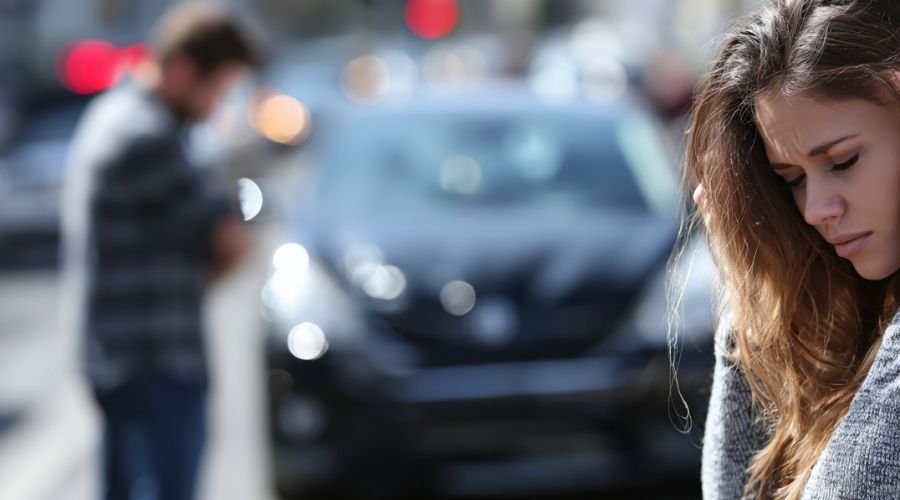 Primer plano de dos coches detenidos tras una colisión por alcance; un conductor con aspecto estresado mientras comprueba los daños. El tráfico se ve borroso al fondo. Luz del día. Escenario urbano realista de California. Se hace hincapié en la responsabilidad y la tensión.