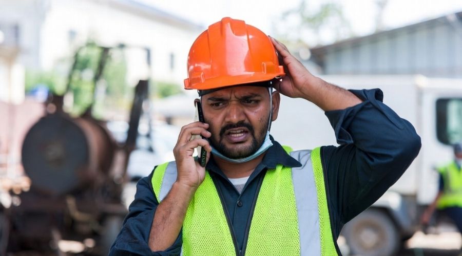 Un trabajador realiza rápidamente una llamada telefónica tras una lesión, expresión de preocupación, entorno laboral ligeramente borroso, sensación de urgencia, estilo realista.