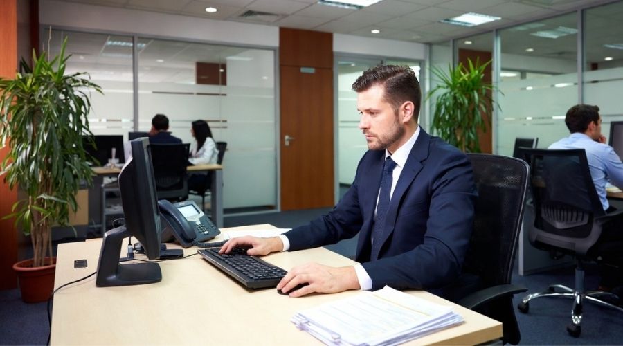 A corporate insurance office scene with an adjuster reviewing claim files on a computer, focused expression, modern office environment, subtle serious tone, symbolizing profit-driven decisions