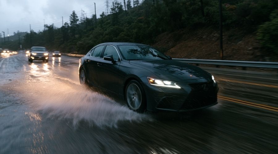 Cómo las condiciones climáticas contribuyen a los accidentes automovilísticos en California 1 Un sedán realista sufre aquaplaning en una carretera californiana empapada por la lluvia, el agua sale disparada de los neumáticos, el conductor lucha por mantener el control, los faros borrosos se reflejan en el pavimento mojado, condiciones climáticas dramáticas, estilo fotoperiodístico, ultrarrealista.
