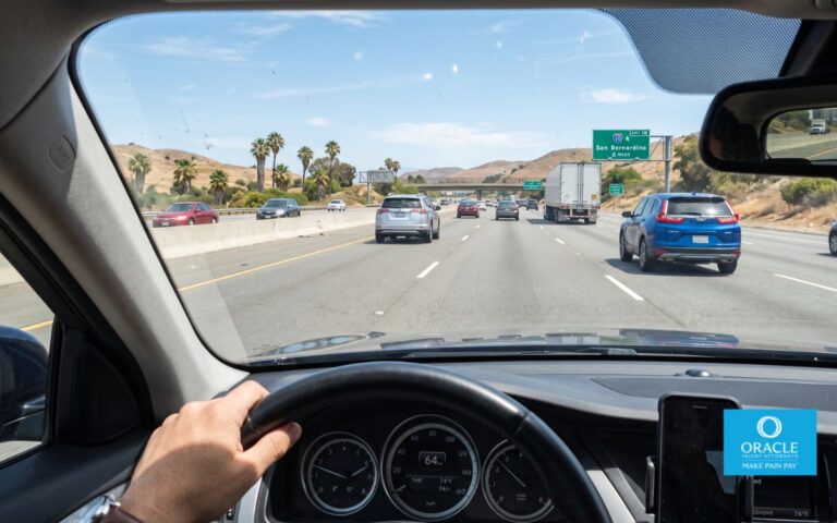 A driver's point-of-view shot through a windshield showing a generous, safe gap between the driver's car and several vehicles ahead on a California highway, daylight. No faces.
