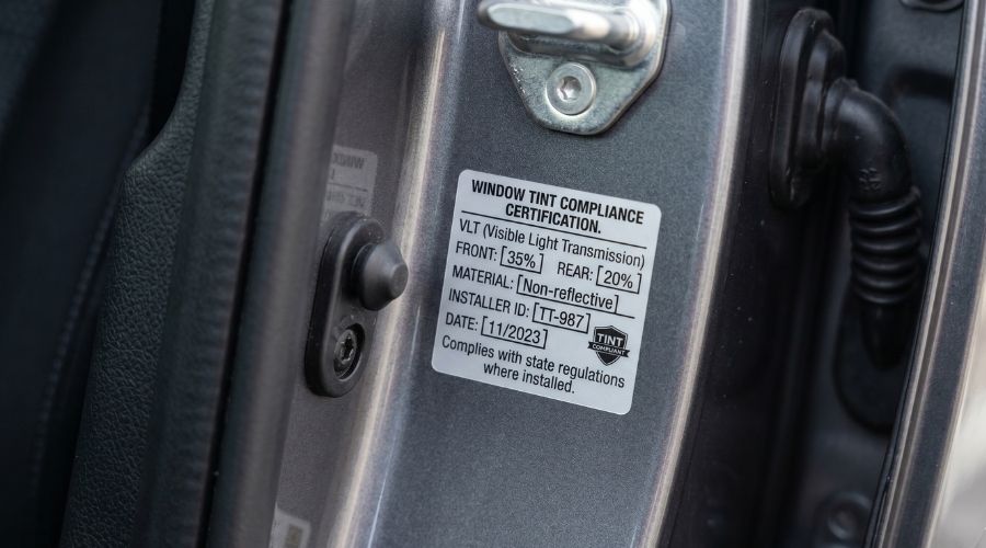 Common California Tint Law Violations and Their Consequences 2 A small certification sticker on a car door jamb, close-up macro shot, representing the tint compliance label requirement. Neutral lighting.