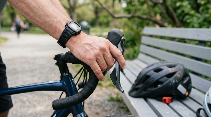 A close-up of a cyclist's hand on a handlebar with a helmet     visible nearby on a bench — representing the choice to wear     or not wear a helmet. Neutral, daylight setting.