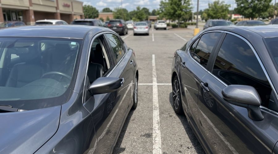 A side-by-side comparison shot: one car window with light,
     legal-looking tint and another with very dark tint, parked
     side by side in a daylight parking lot. No faces visible.