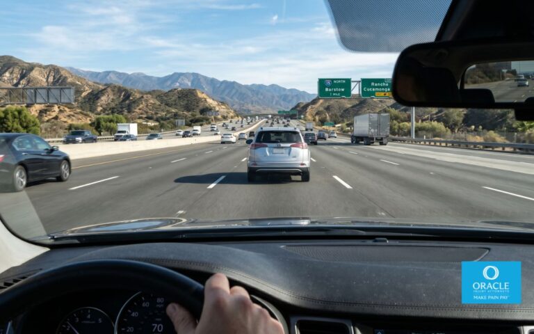 A driver's point-of-view shot through a windshield showing a clear, generous gap between the driver's car and the vehicle ahead on a California freeway, daylight. No faces visible.