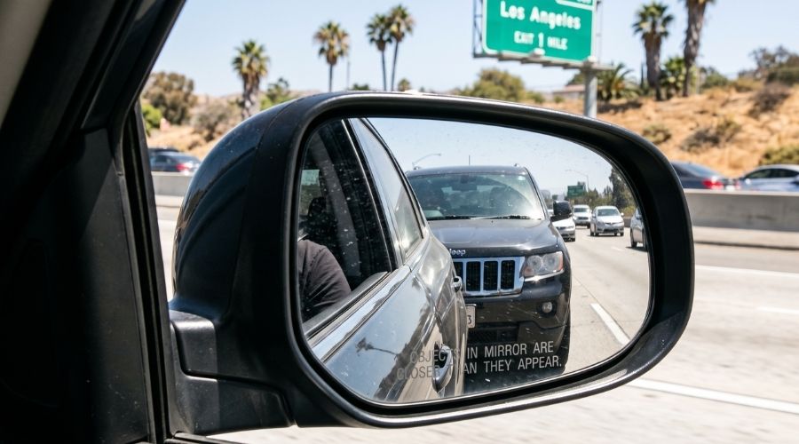  A close-up of a side mirror showing a vehicle following     closely behind, representing the tailgating scenario from the     lead driver's perspective. No faces clearly identifiable.