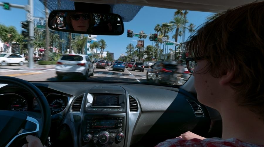Un conductor adolescente maneja con precaución el denso tráfico de Anaheim mientras un padre lo supervisa desde el asiento del pasajero, entorno urbano realista, semáforos e intersecciones concurridas, ambiente educativo de conducción, fotorrealista.