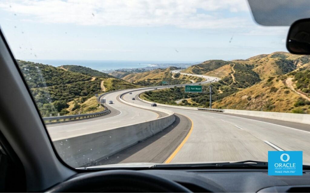 A street-level shot from inside a vehicle on the 73 Toll Road looking forward, the winding road curving ahead through rolling hills, daylight, light traffic visible in the distance. No accident depicted, no faces visible. Conveys the high-speed, winding hillside character of the corridor from a driver's perspective.