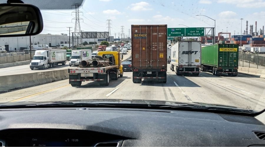 A driver's point-of-view shot from a passenger vehicle
     on the 710 Freeway, looking forward at heavy commercial
     truck traffic ahead, daylight. Multiple trucks visible,
     no accident depicted, no faces. Represents the industrial
     corridor environment.