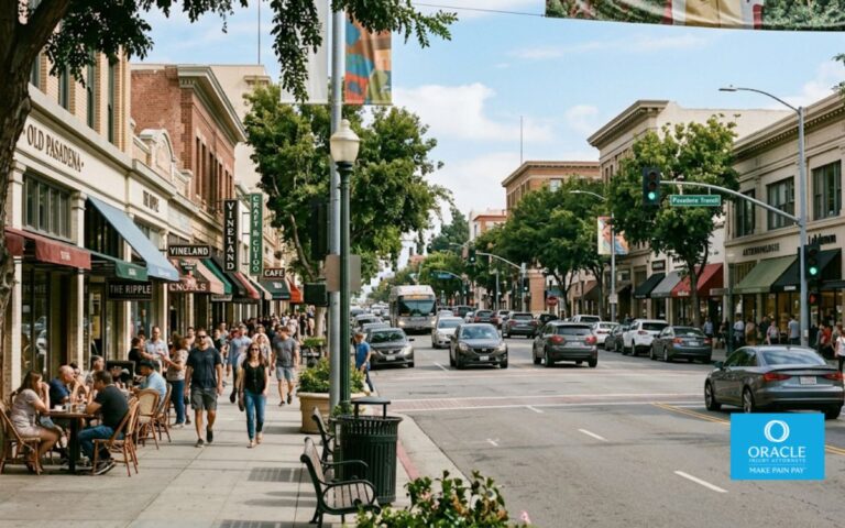 A street-level shot of Colorado Boulevard in Old Pasadena, daylight, wide commercial street visible with pedestrians on sidewalks, storefronts and trees lining both sides, moderate vehicle traffic. No accident, no faces clearly visible. Represents the dense pedestrian-and-vehicle environment of Pasadena's main commercial corridor.