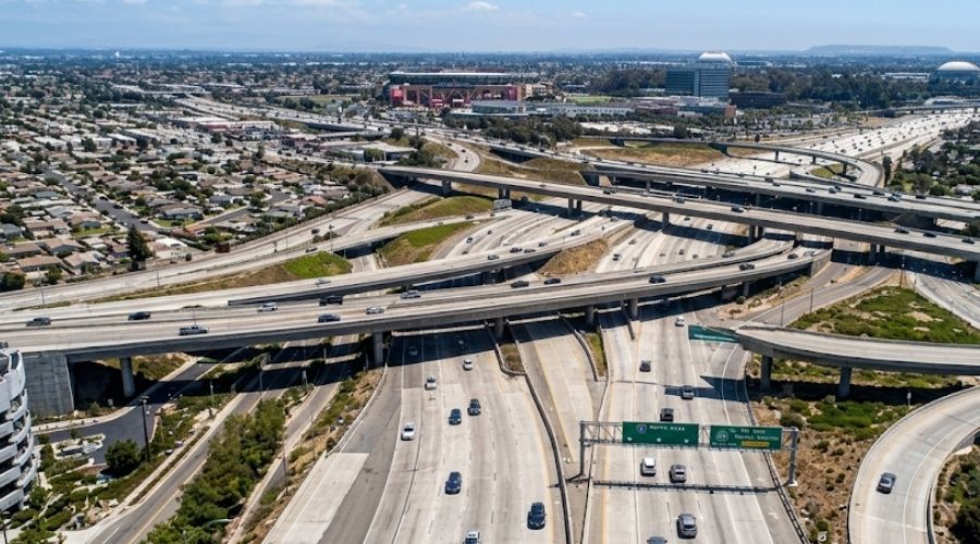 A wide aerial or elevated shot of a complex multi-level     freeway interchange with multiple ramps crossing over each     other, daylight, representing the Orange Crush 5/22/57     configuration. No accident depicted, no faces visible.