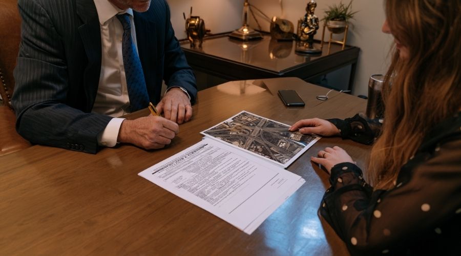  A calm attorney-client consultation: two people at a     conference table reviewing a CHP crash report and aerial     interchange photos. Warm office lighting, no faces clearly     identifiable.