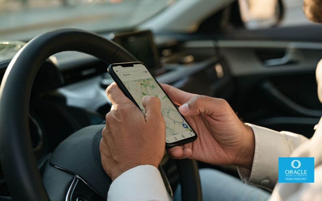 Imagen fotorrealista en primer plano de un conductor de un servicio de transporte compartido que sostiene un teléfono inteligente con una interfaz de navegación y de transporte compartido, estacionado de forma segura después de una colisión. Se aprecian el volante, reflejos realistas, poca profundidad de campo, manos y tablero muy detallados, iluminación natural. Fotografía editorial, sin logotipos ni marcas registradas.