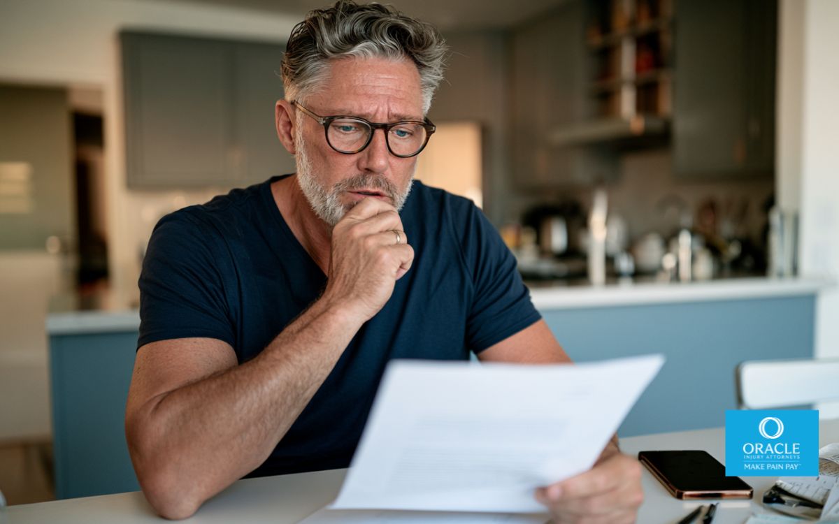 Injured person reviewing an insurance settlement offer at a kitchen table with medical bills and accident paperwork.