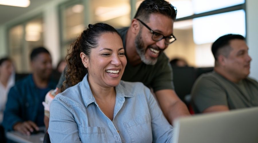 What Benefits Am I Entitled to After a Workplace Injury? 2 Photorealistic editorial photograph of an injured California worker transitioning into a new career, attending a hands-on vocational training class at a modern educational facility. The worker is seated at a computer workstation while an instructor provides guidance, with other adult students learning nearby. A subtle wrist brace suggests the worker can no longer perform their previous physical job. The atmosphere is optimistic and practical, communicating retraining, education, career transition, and rebuilding employment after an injury. Authentic adult education environment, diverse California workforce, natural daylight, realistic clothing and technology, premium documentary photography, cinematic realism, blue and warm neutral tones, no visible text, logos, or watermarks, horizontal 16:9.