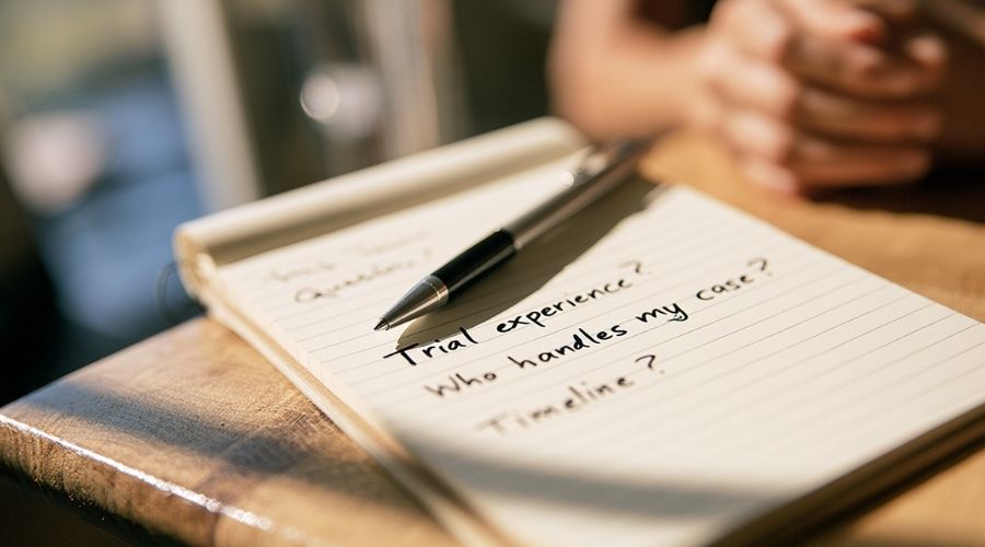  A close-up of a notepad with handwritten questions on it
     — "Trial experience?", "Who handles my case?", "Timeline?"
     — a pen resting across the page. No faces, soft indoor
     lighting. Represents the prepared client interviewing
     the attorney during the consultation.