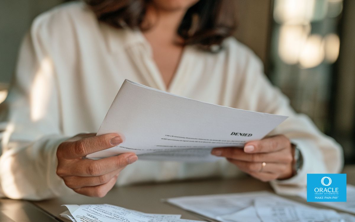 A close-up of a person's hands holding a printed denial letter, the word "DENIED" partially visible on the page, seated at a desk with medical bills nearby. No face visible, soft indoor lighting. Represents the moment of receiving a denial and the need to understand it before responding