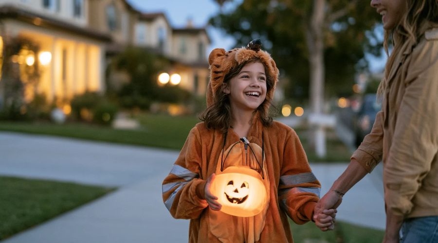 Child wearing reflective tape on a Halloween costume and carrying a flashlight while walking with a parent at dusk.